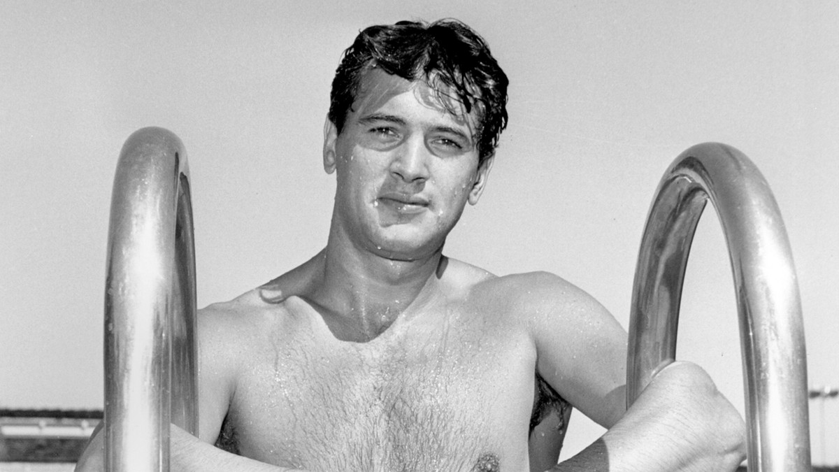 Ett svartvitt arkivfoto av Rock Hudson på toppen av en poolstege.