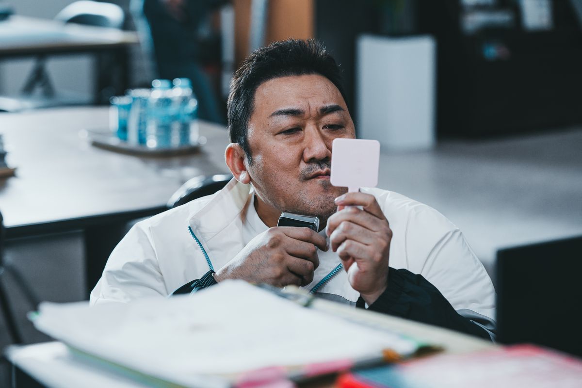 Ma Dong-seok håller upp en handhållen spegel medan han rakar ansiktet vid sitt skrivbord i The Roundup: No Way Out.