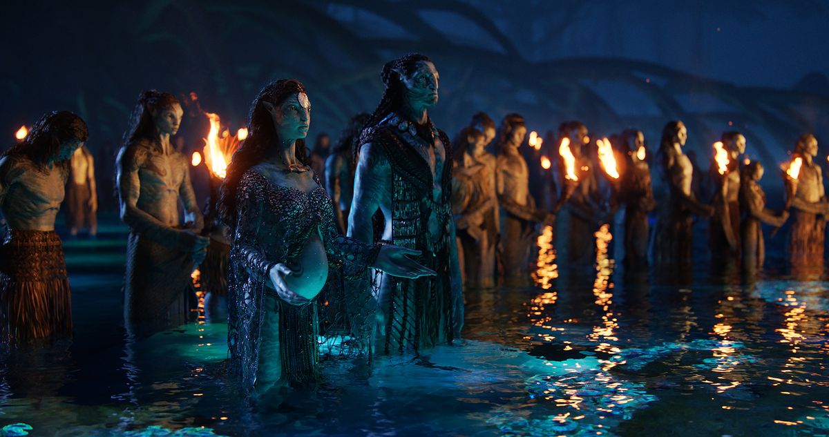 En grupp Na'vi samlas på natten för en ceremoni, står till knä djupt i vattnet och håller facklor, med Na'vi spelad av Kate Winslet och Cliff Curtis som ordförande i Avatar: The Way of Water