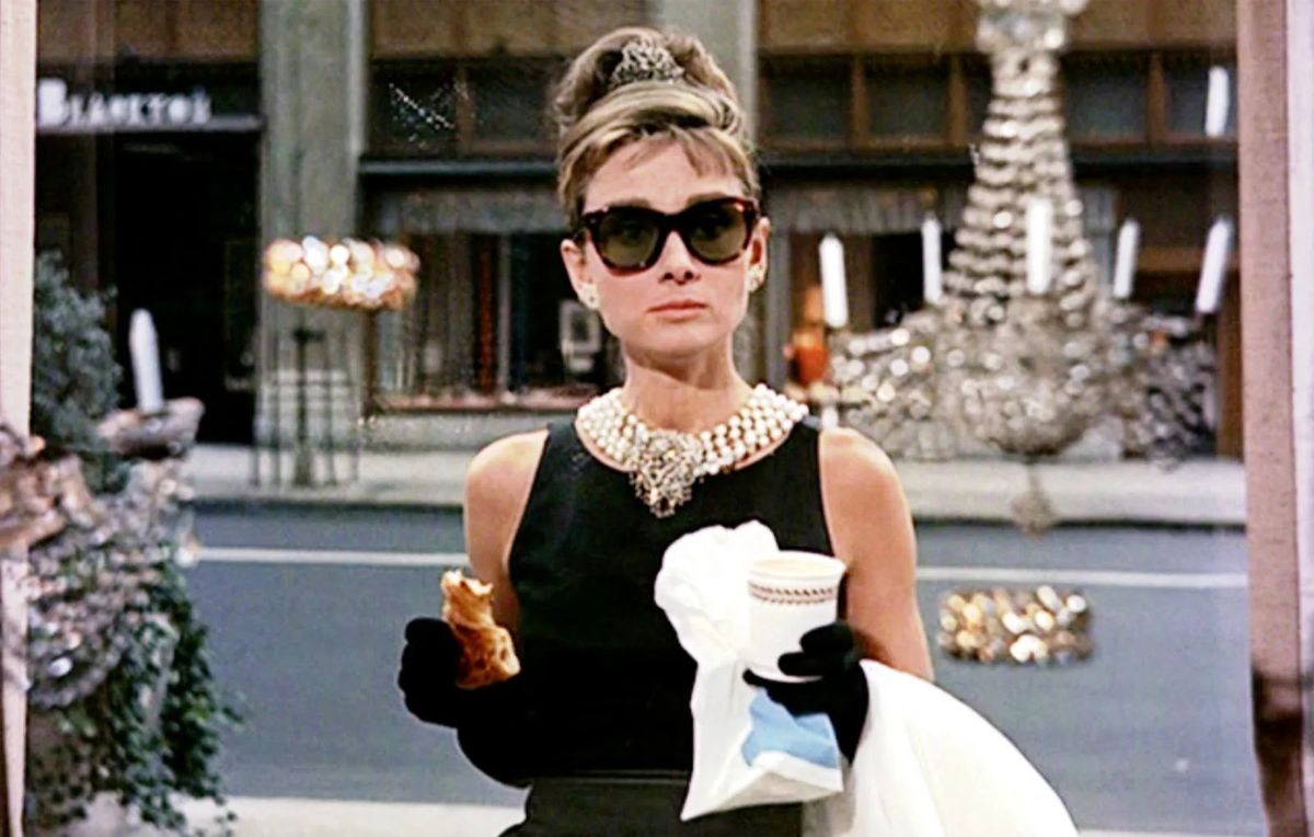 Holly Golightly, som spelas av Audrey Hepburn, i Breakfast at Tiffany's, iklädd sin ikoniska svarta klänning, med stora solglasögon och ett pärlhalsband. 