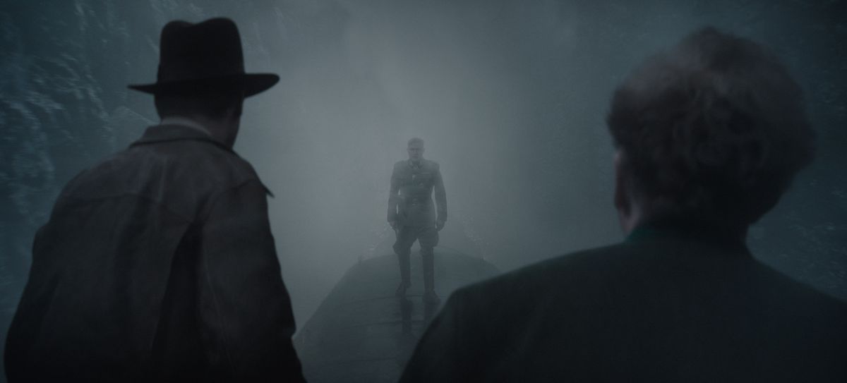 Indiana Jones (vänster) och Basil Shaw (höger), med ryggen mot betraktaren, konfronterar skurken Jurgen Voller, silhuettad i dimma, ovanpå ett tåg i rörelse.