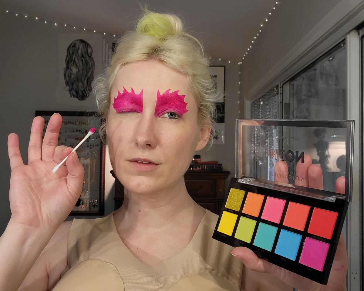 The author holding up a brightly colored eyeshadow palette, and a Q-tip with bright pink on it.