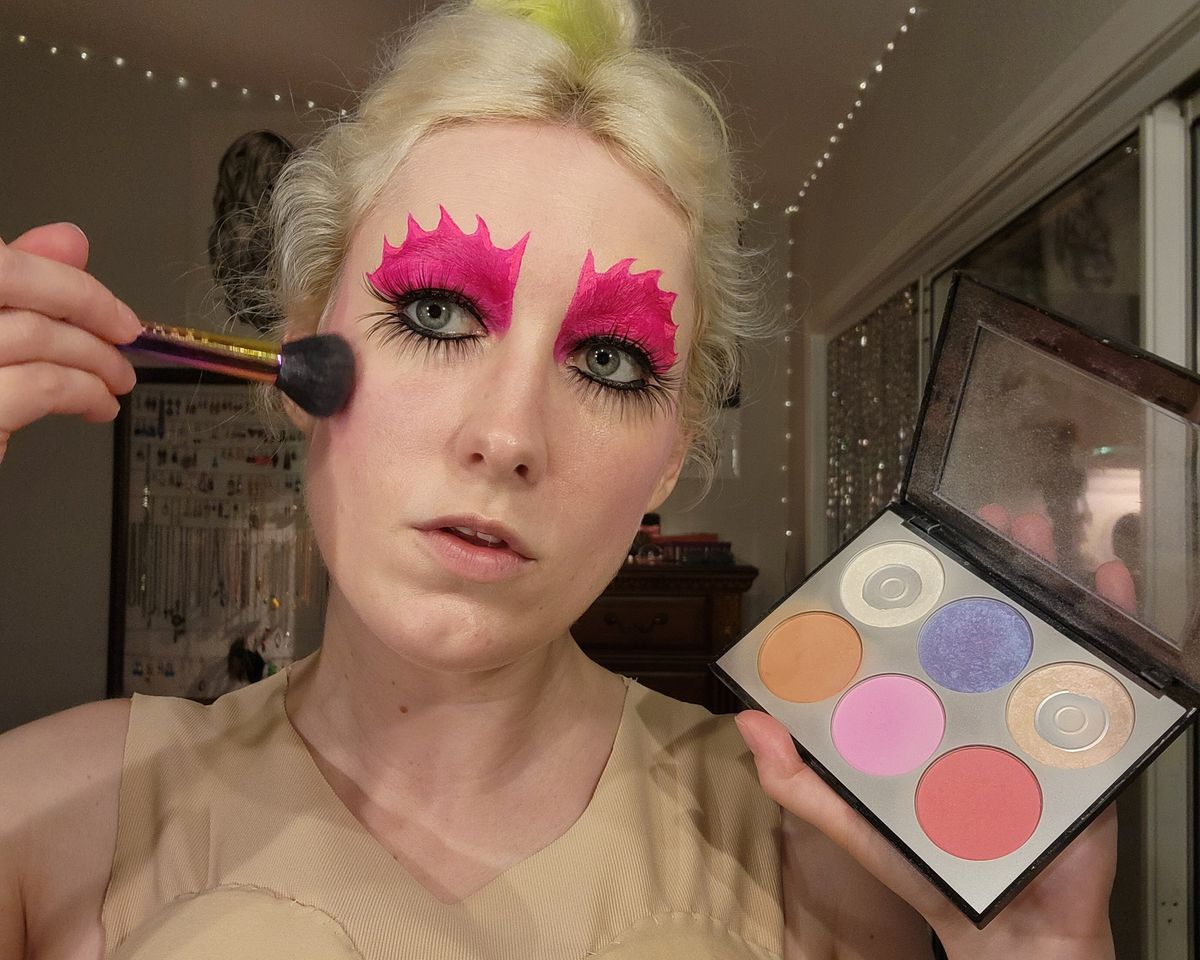 The author putting blush on and showing off the makeup palette