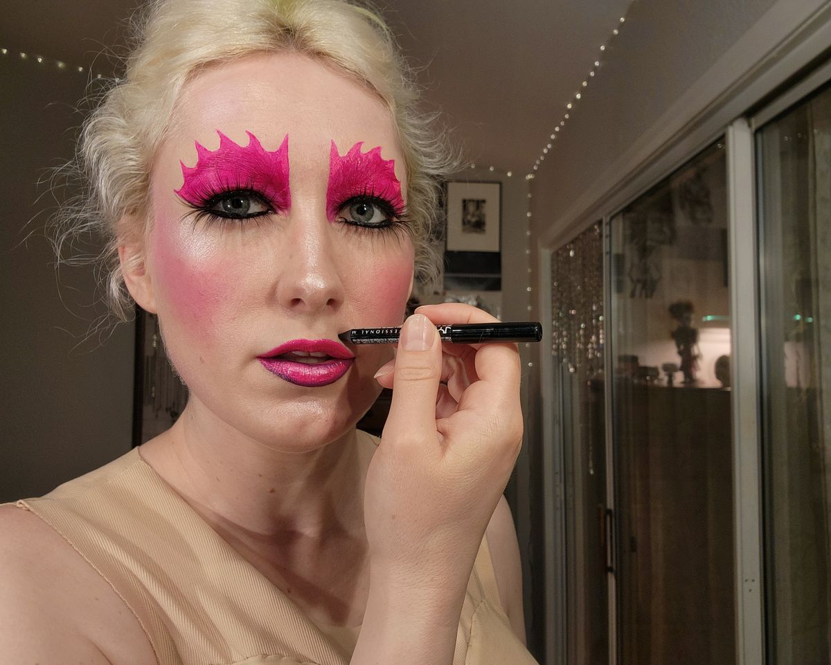 The author with pink lips, with a highlighter on top, black liner around the bottom lip, drawing a fake mole on