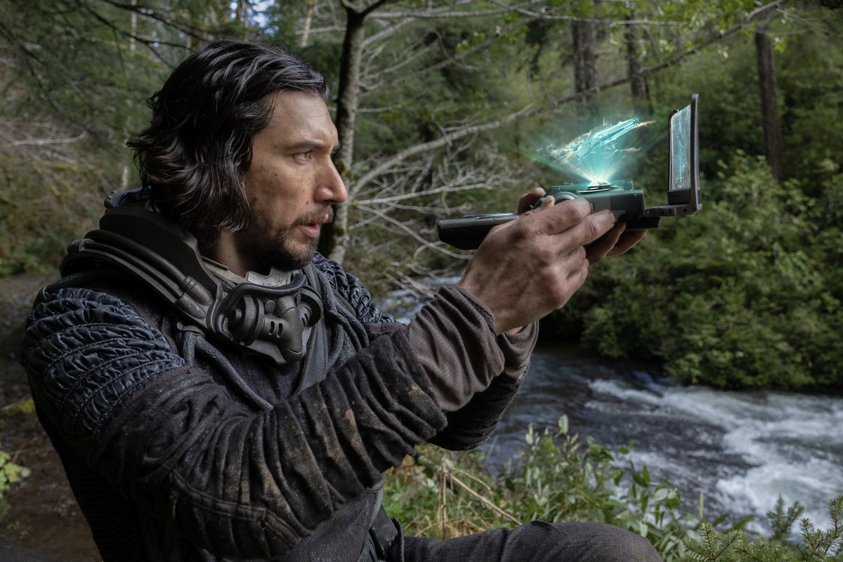 Adam Driver's Mills håller upp ett 3D-hologram av sitt skepp medan han navigerar i jordens förhistoriska djungler år 65