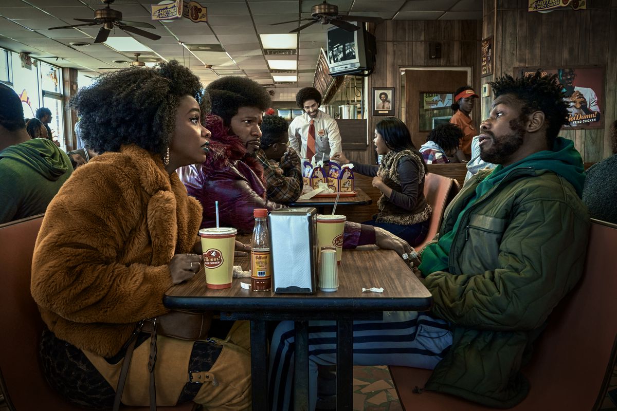 (V till höger) Teyonah Parris som Yo-Yo, Jamie Foxx (producent) som Slick Charles och John Boyega som Fontaine som sitter mitt emot varandra på en snabbmatsrestaurang i They Cloned Tyrone.