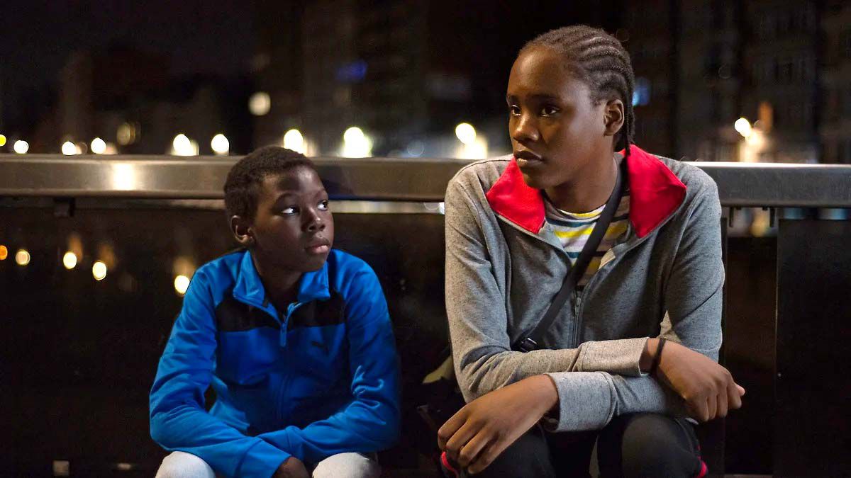 En ung pojke (Pablo Schils) och en ung kvinna (Mbundu Joely) sitter på en bänk på natten i Tori och Lokita.