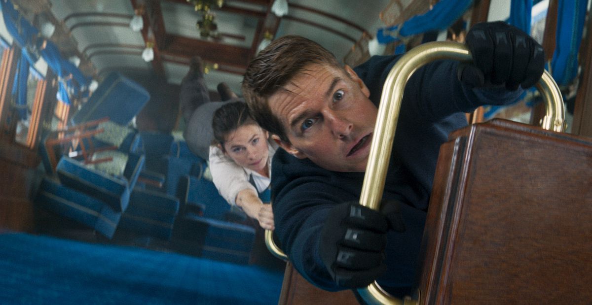 Tom Cruise som Ethan Hunt håller fast i ett räcke i en tågvagn som vänds vertikalt när Hayley Atwell håller fast vid honom i Mission: Impossible — Dead Reckoning Part One