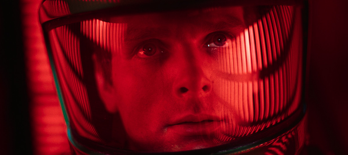 En man i en rymdhjälm stirrar upp på rader av röda upplysta ljuspelare.