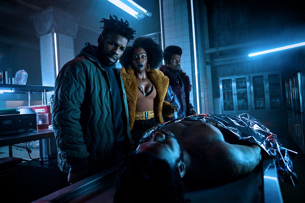 (V till R) John Boyega som Fontaine, Teyonah Parris som Yo-Yo och Jamie Foxx (producent) som Slick Charles som stirrar ner på en död kropp på ett undersökningsbord i They Cloned Tyrone.