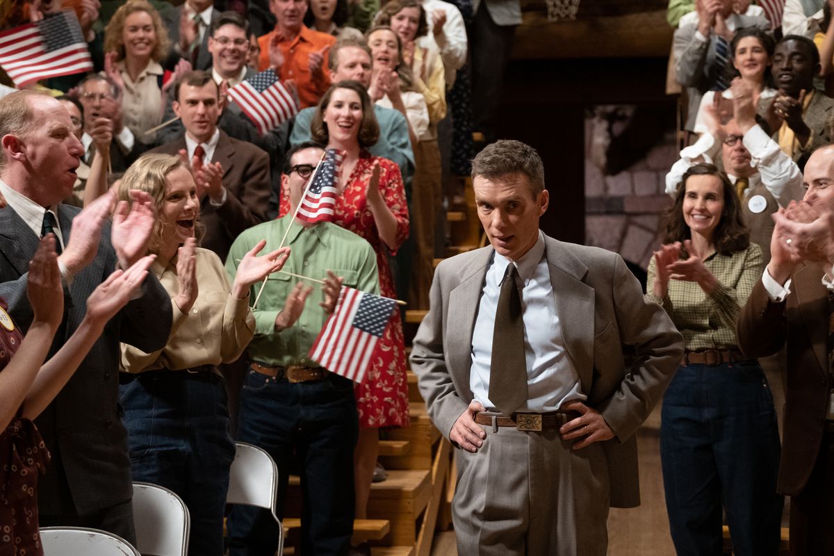 Cillian Murphy som Oppenheimer ser orolig ut, händerna på höfterna, innan en jublande publik vinkar Stars and Stripes