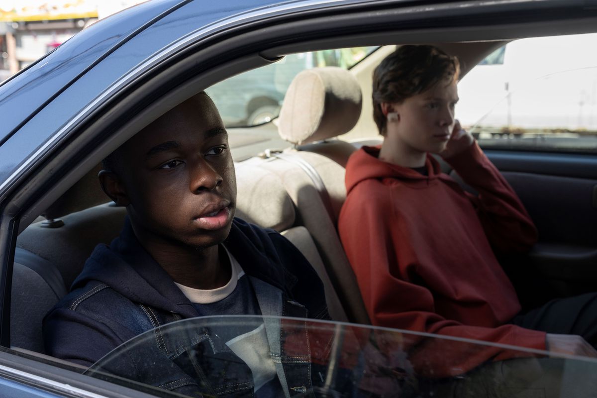 Gerald Jones, Lucian Zanes sitting in the back of a car as two characters on the run from a crime family