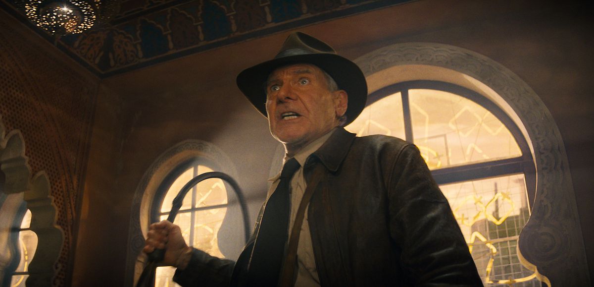 Indiana Jones (Harrison Ford) ser upprörd och skakad ut när han lyfter sin varumärkespiska i ett slagsmål medan han står silhuettad mot ett ljust fönster i Indiana Jones and the Dial of Destiny