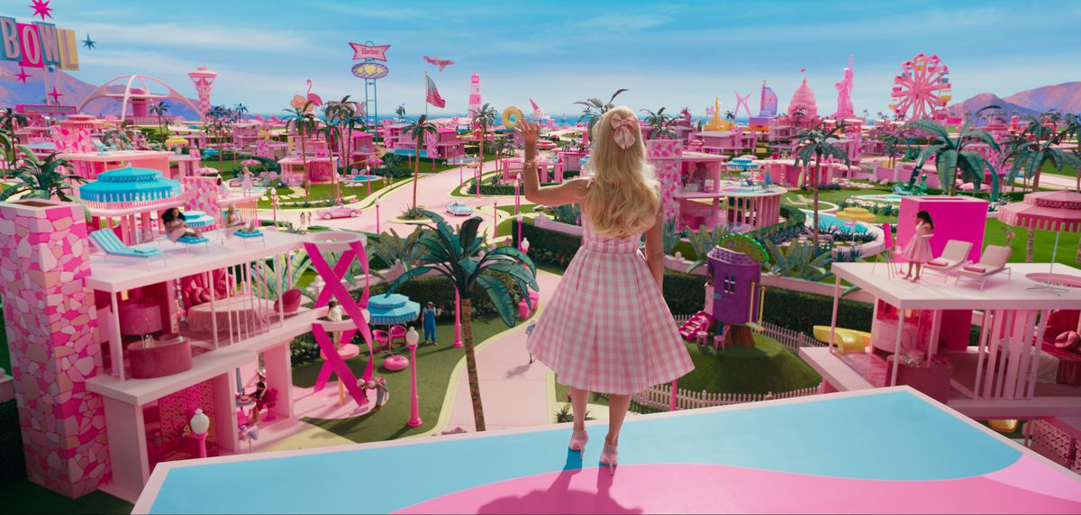 Barbie (Margot Robbie), sedd bakifrån, står på det rosa och blå plasttaket på sitt DreamHouse och tittar ut över alla andra rosa plast DreamHouses från de andra Barbiesna i Barbieland, i live-action-filmen Barbie 2023