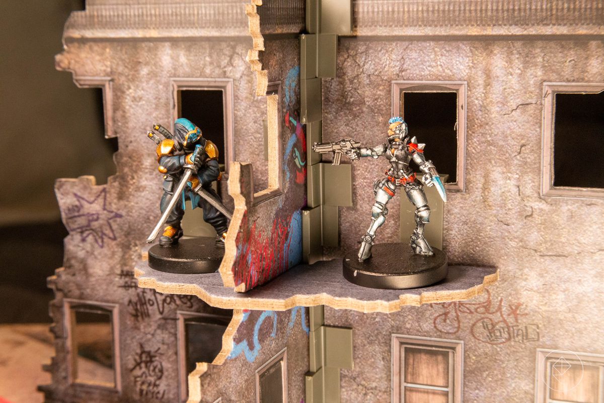 Två figurer står inuti en kartongmockup av en förstörd stadsbyggnad.