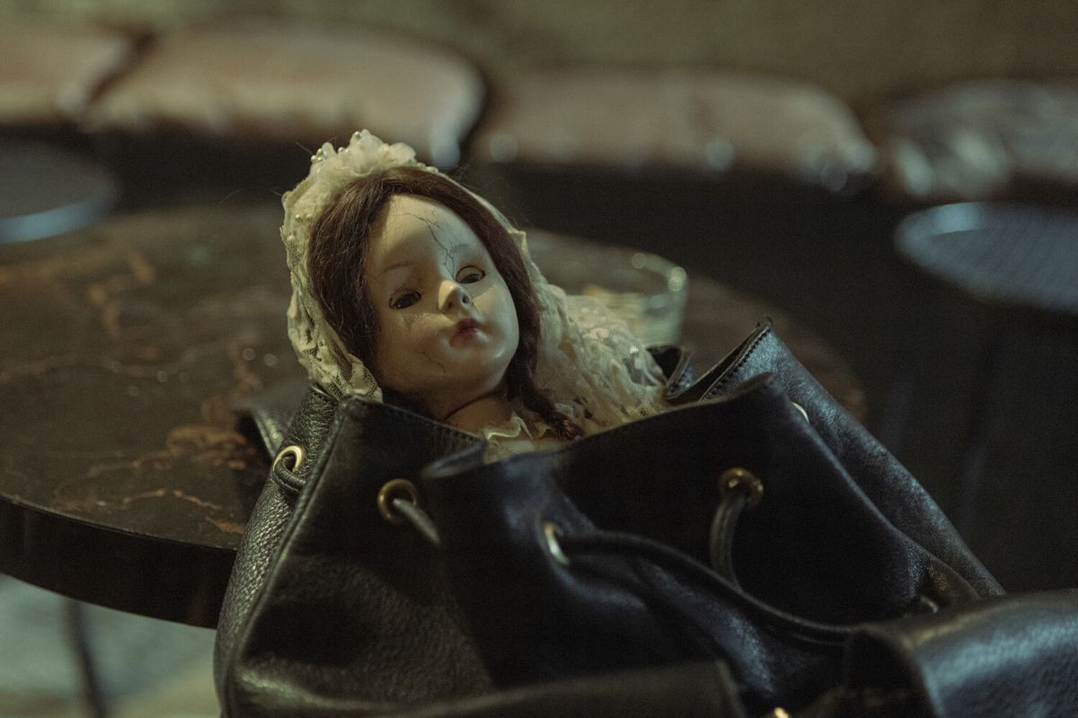 En läskig docka klädd i nattvardsdräkt toppar ur en handväska i The Communion Girl.