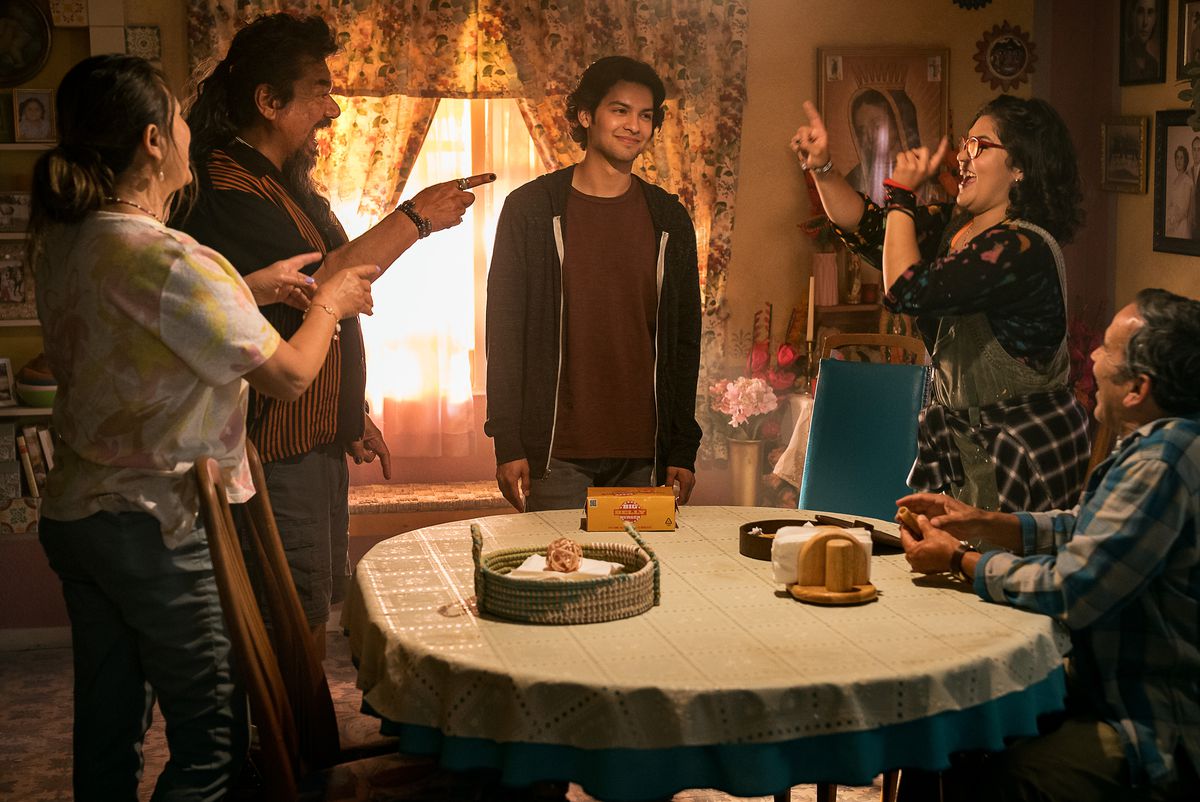 Jaime Reyes står bakom familjens middagsbord fåraktigt medan hela hans familj lekfullt peppar honom i filmen Blue Beetle