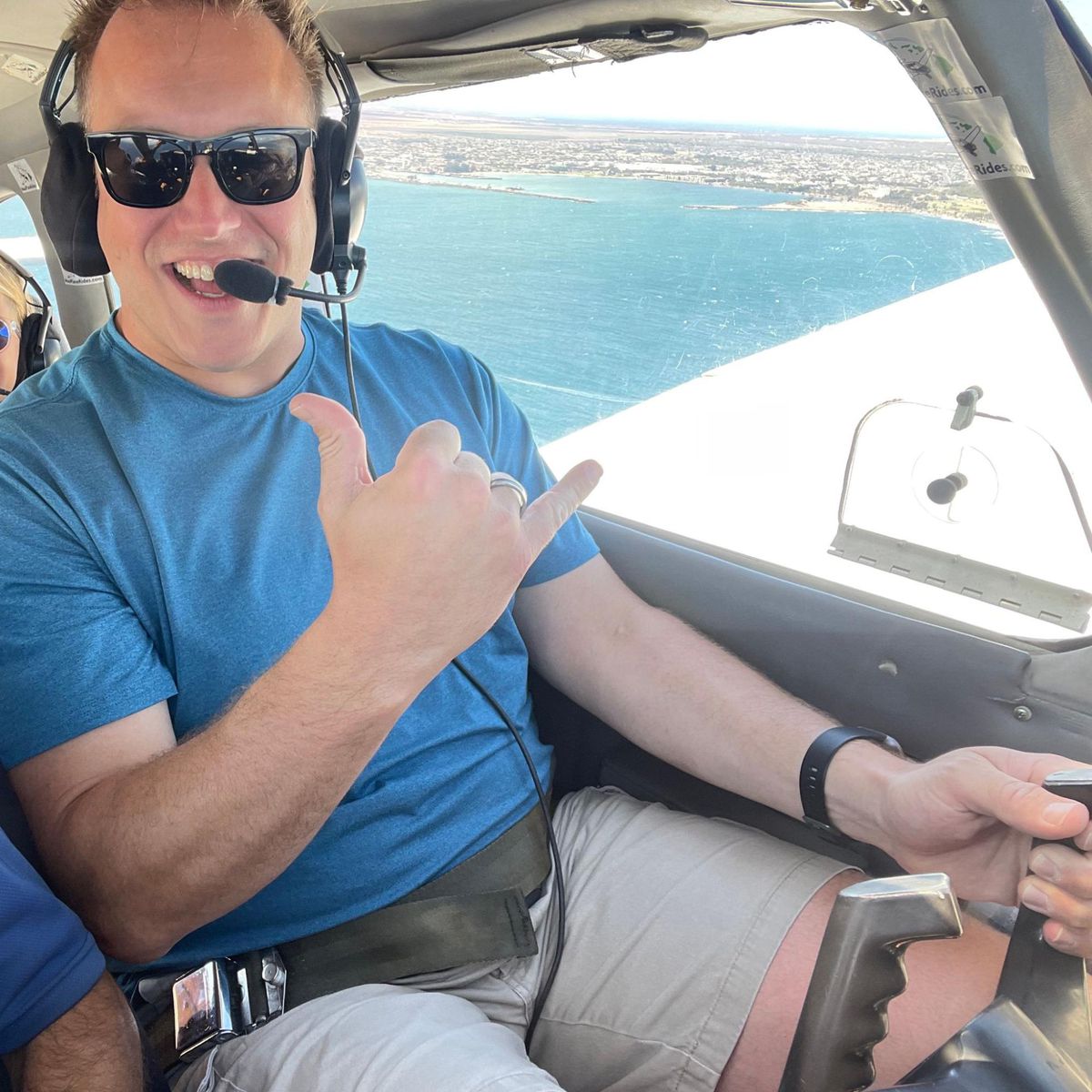 A photo of the author grinning, holding up his thumb and pinky to the camera, and not crashing the small plane he’s currently flying over the ocean during a training flight over Kauai in 2022.