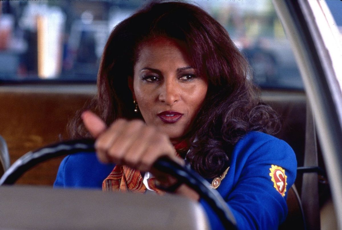 iklädd en blå flygvärdinnajacka sitter Jackie (Pam Grier) bakom ratten i en bil i Jackie Brown