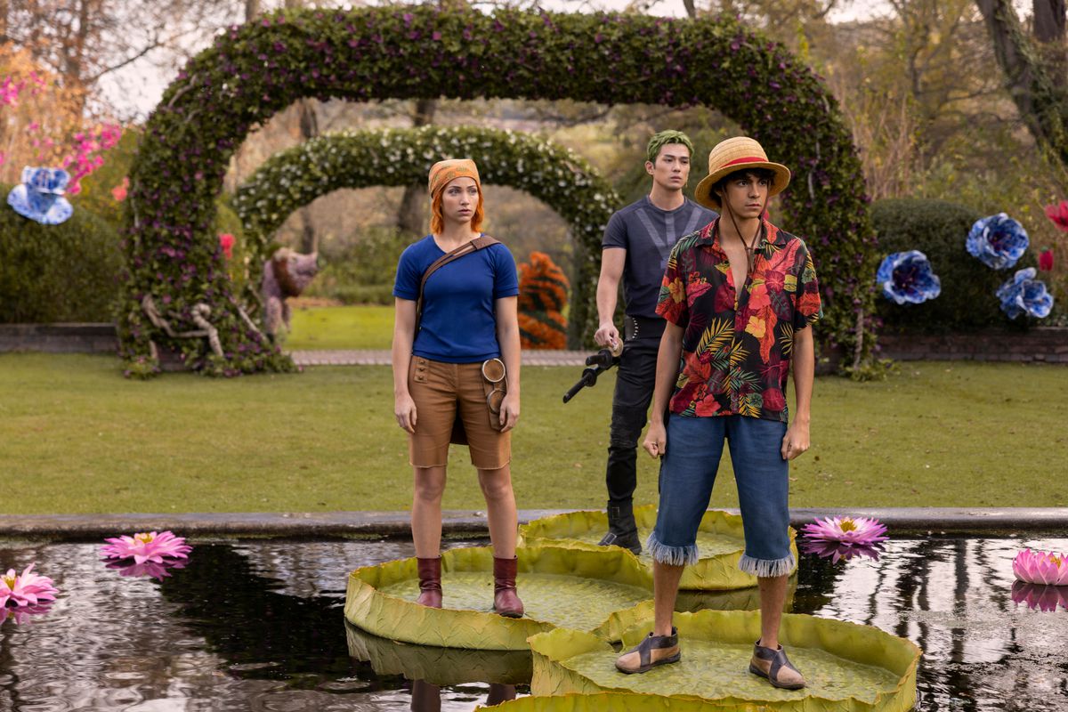 Nami (Emily Rudd), Zoro (Mackenyu) och Luffy (Iñaki Godoy) står på liljekuddar i en färgstark trädgård i Netflix One Piece