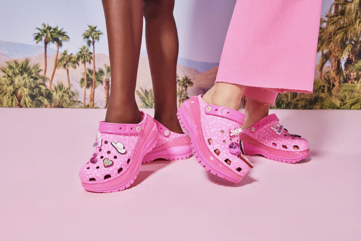En svart person och en vit person som modellerar de nya Barbie Crocs.