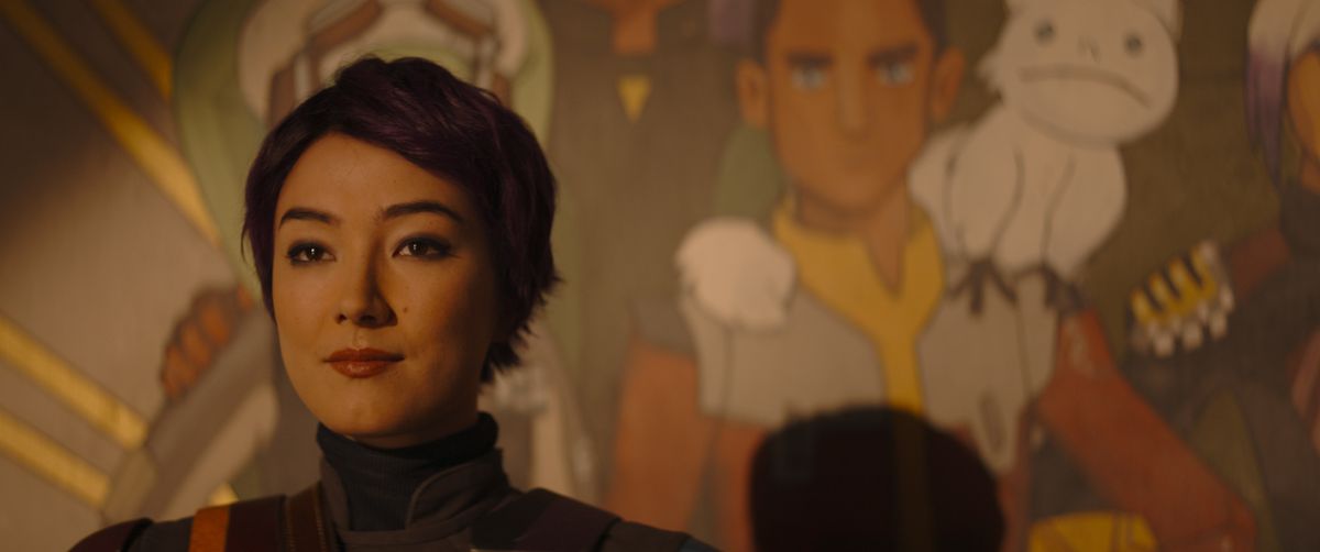 Sabine Wren (Natasha Liu Bordizzo), med kort hår, står framför sin väggmålning av besättningen på Ghost — Ezra är tydligt synlig — i Star Wars: Ahsoka.