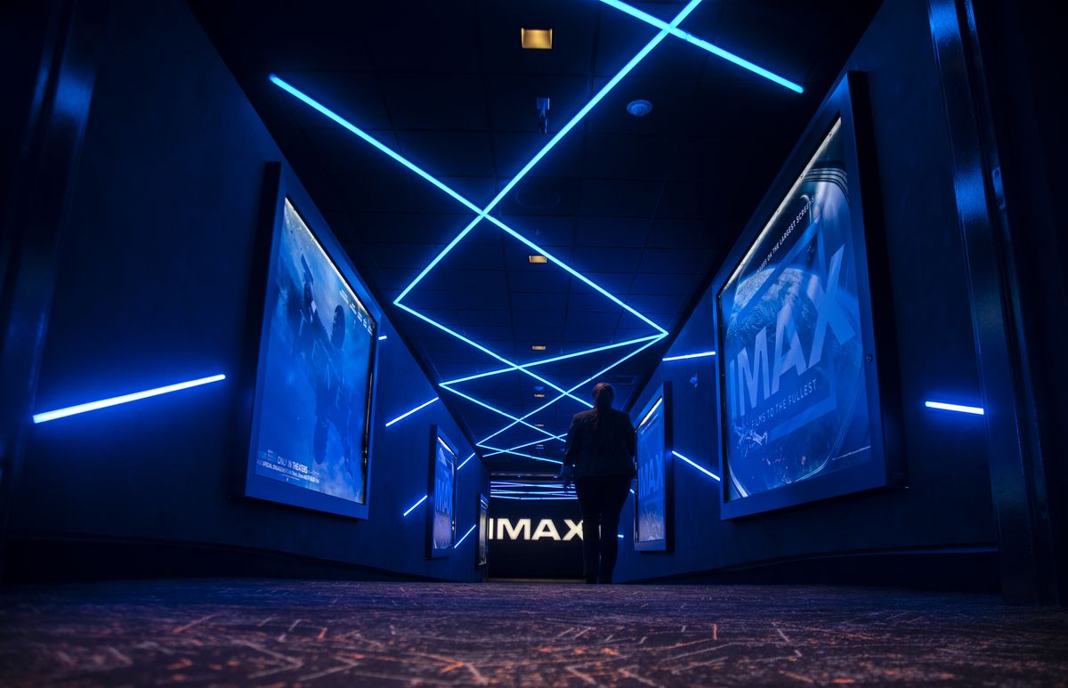 In an undated file photo, a silhouetted figure walks down a hallway at the Regal Spectrum Irvine in California, with rows of screens on both walls showing the IMAX logo in blue