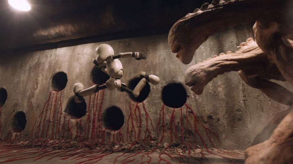 En skärmdump av Junk Head som jagas av två stora, långhalsade varelser i en korridor med underliga hål som sipprar röda ådror.