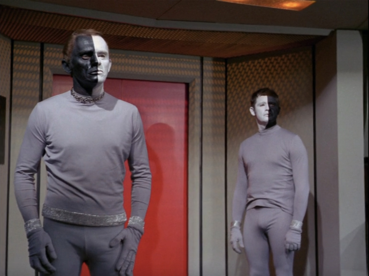 Två främmande män, en med sin vänstra halva svart och sin högra vit, den andra omvänd, står på bron till Enterprise i en stillbild från TOS-avsnittet 