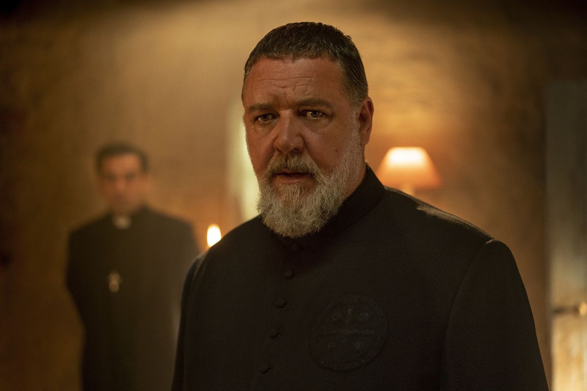 Russell Crowe as Father Gabriel Amorth in The Pope’s Exorcist facing the camera with short hair and a glowing orange light behind him