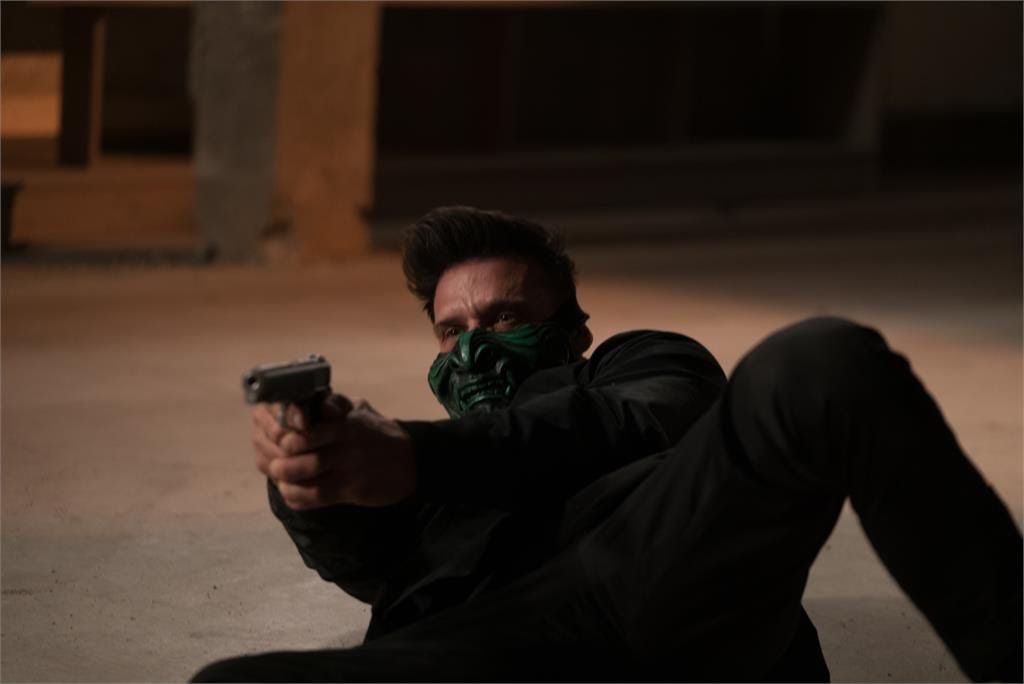 Frank Grillo, klädd i en djävulskt grön mask över den nedre halvan av sitt ansikte, siktar på en pistol medan han ligger på marken i King of Killers.