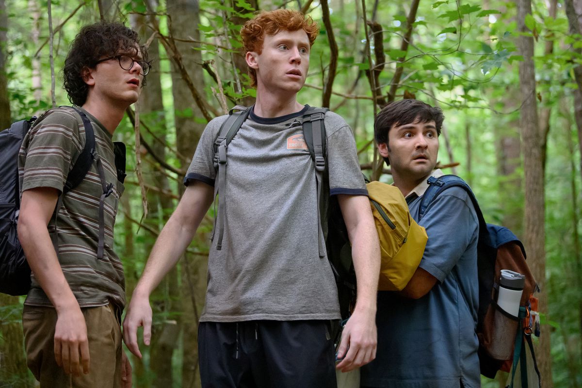 The comedy trio Ben Marshall, John Higgins, and Martin Herlihy wear backpacks and look surprised and frightened in the woods in Please Don’t Destroy: The Treasure of Foggy Mountain.