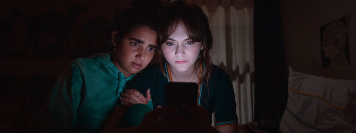 Emilia Jones and Geraldine Viswanathan huddle together and look at a phone screen in Cat Person.