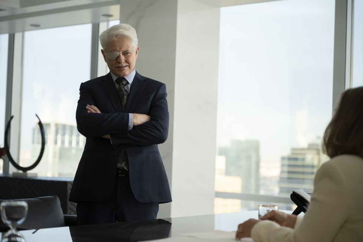 Dave Foley, with bright white hair and a gray eye patch, crosses his arms in an office in Fargo season 5.