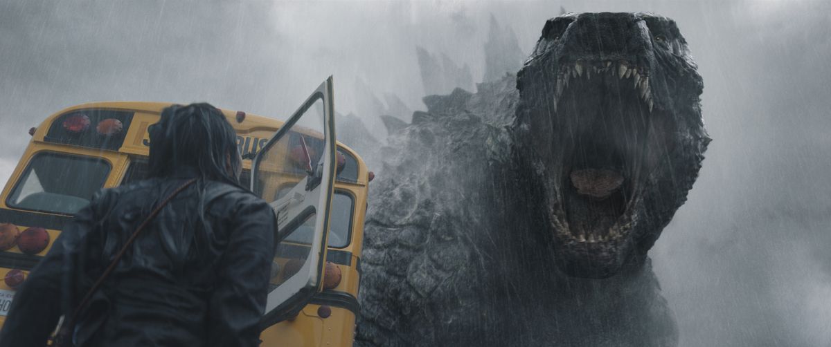 Godzilla roaring in the rain toward a person standing near a bus with their back to the camera in Apple TV Plus’ Monarch: Legacy of Monsters