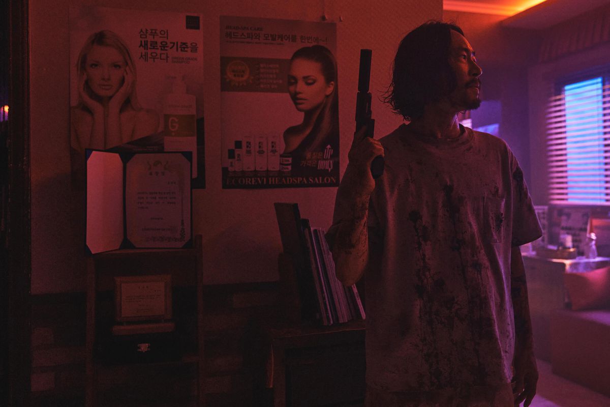 Frank (Ryu Seungbum) står i ett svagt upplyst rum och håller en pistol med en ljuddämpare