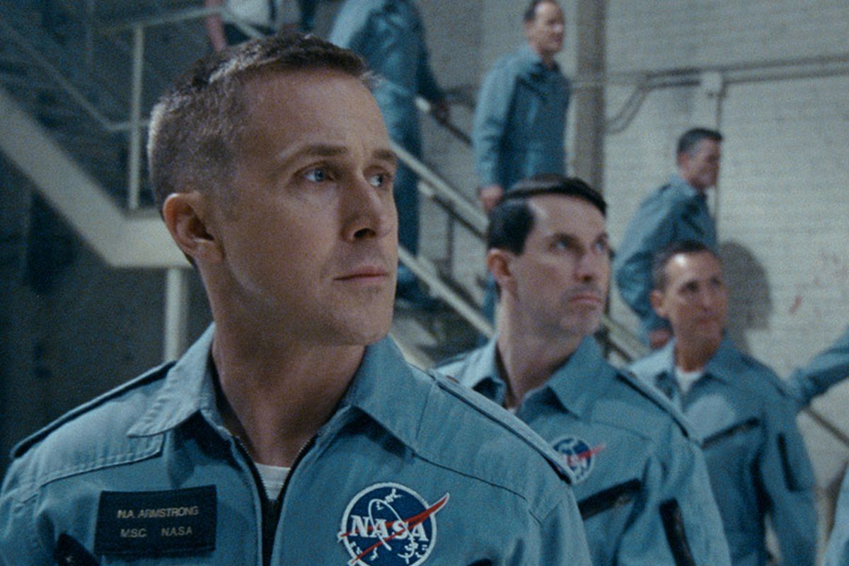 Ryan Gosling som Neil Armstrong som står bredvid sina medastronauter i blå uniform i First Man.