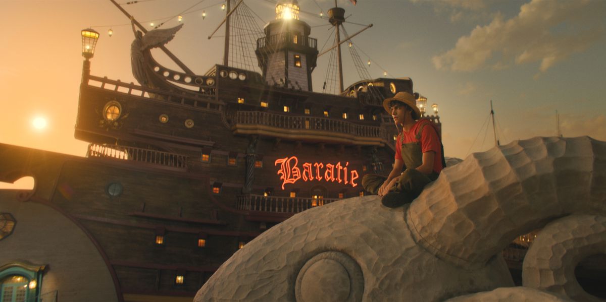 Luffy (Iñaki Godoy) sitter på galjonsfiguren på sitt skepp framför Baratie-skylten