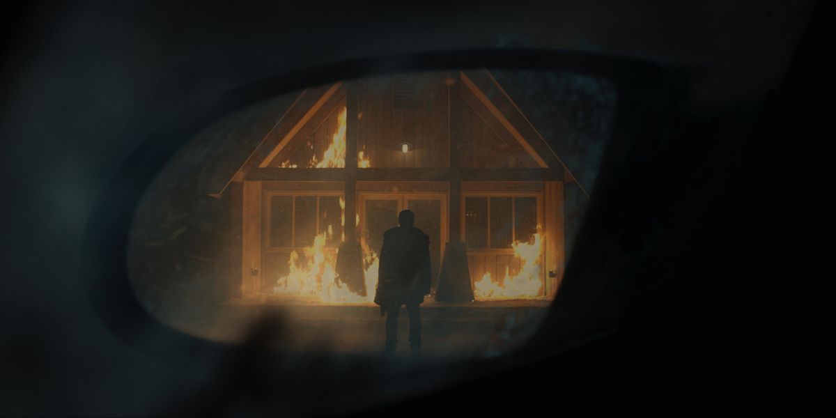 Bilden av en person som står framför en brinnande byggnad reflekteras i en backspegel.