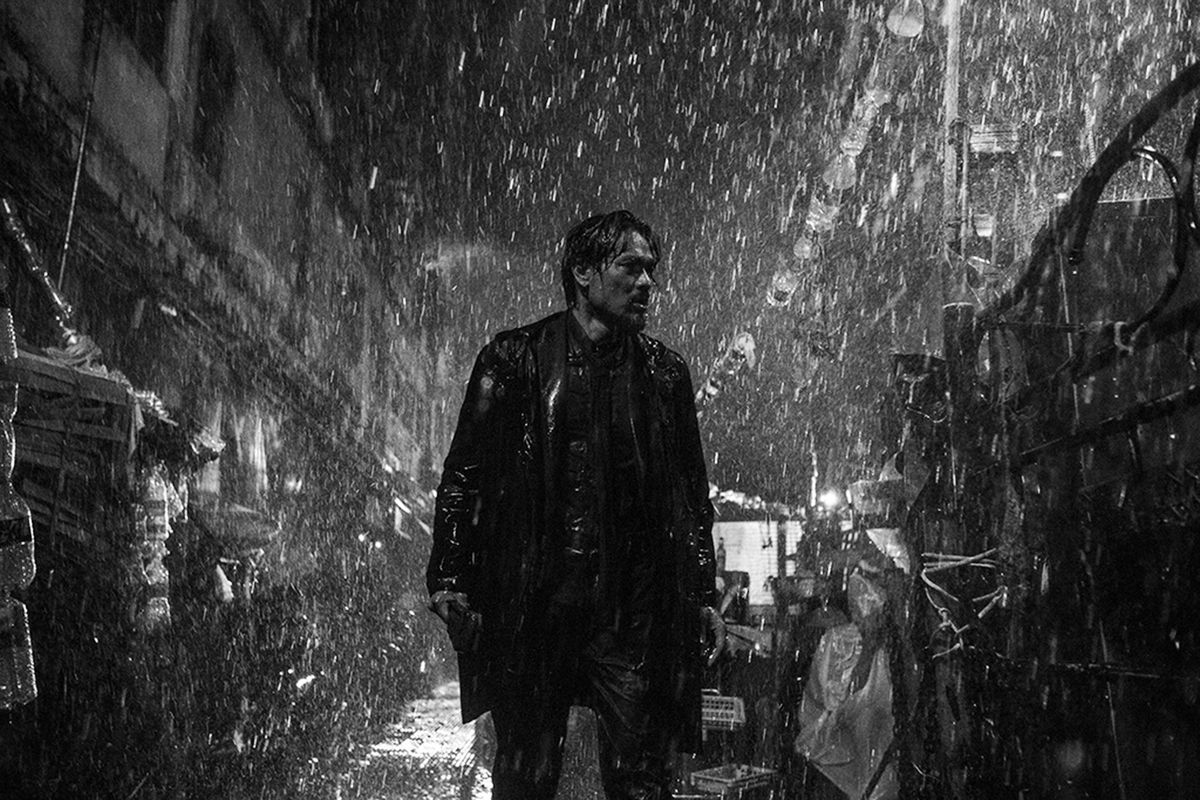 En man går genom en smal, regnig gata, i en svartvit bild från Limbo.