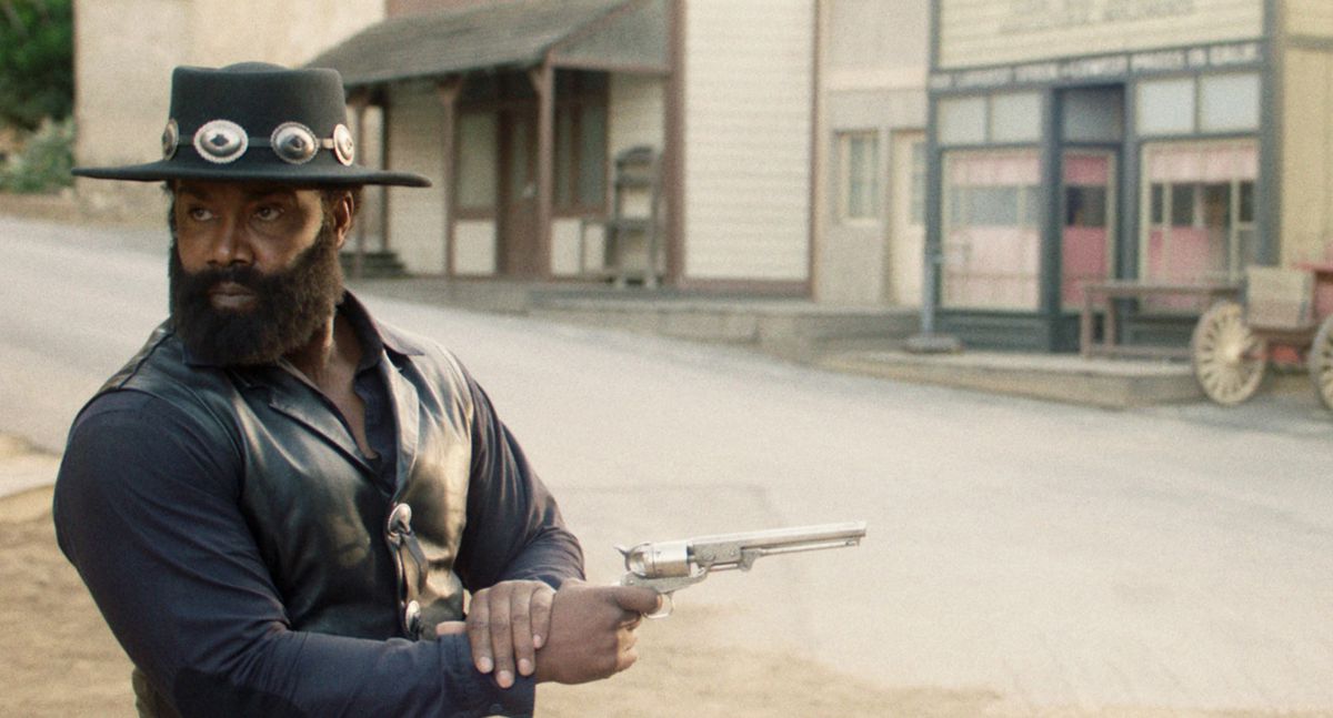 Michael Jai White tittar åt andra hållet medan han avfyrar sin pistol på en tom västerländsk gata i Outlaw Johnny Black.