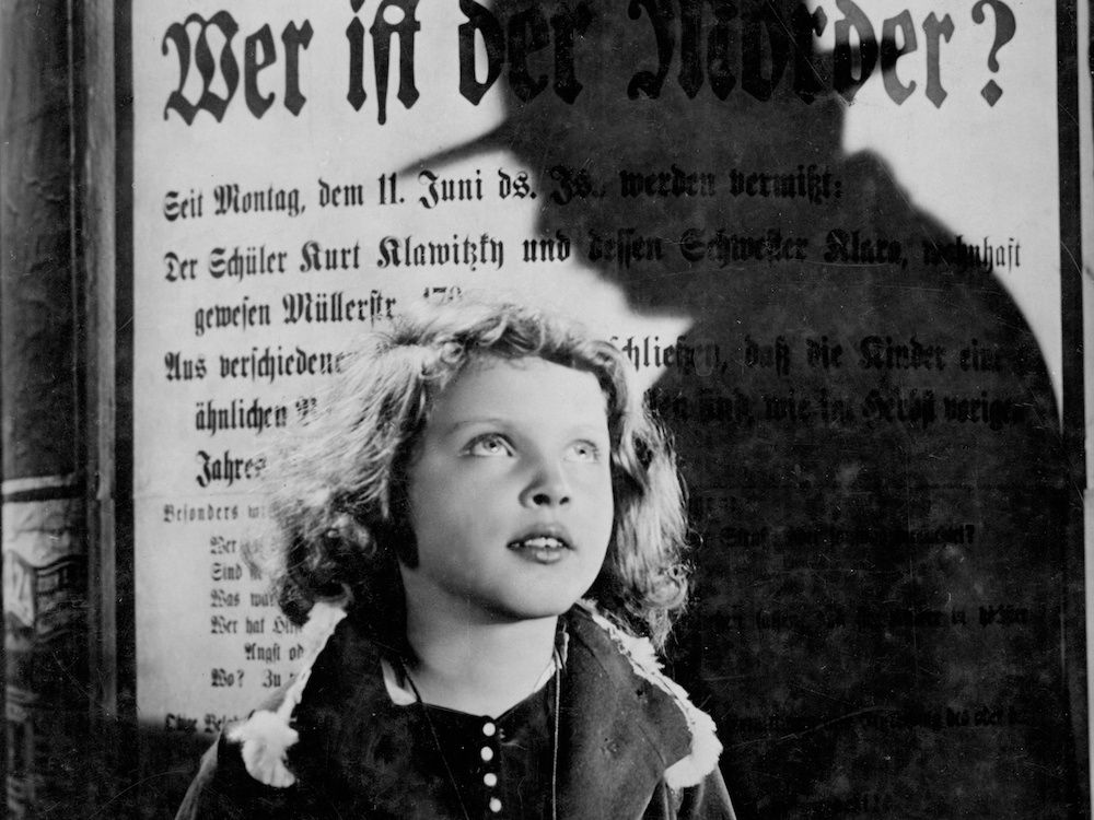 Inge Landgut as Elsie Beckmann peering up at a man silhouetted against a wanted poster in M.
