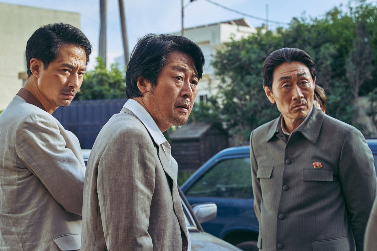 South Korean diplomats wear grey suits while the North Korean diplomat wears his uniform, as they  look off-camera in Escape from Mogadishu.