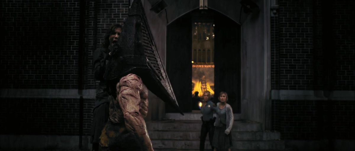 Pyramid Head (som har en pyramid för ett huvud) från Silent Hill-filmen står framför en kyrka medan han håller en kvinna i halsen