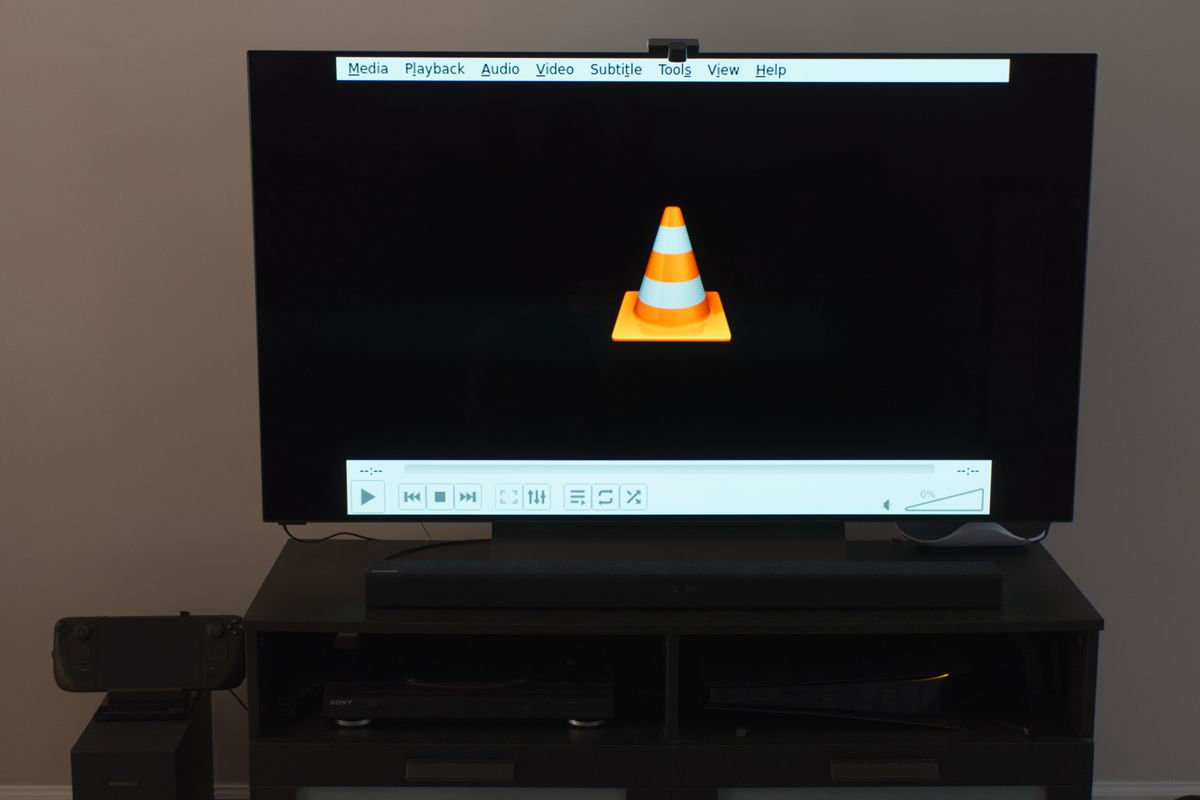 Ett foto av en 55-tums tv med VLC mediaspelare-appen som visas på den.  Den drivs av ett Steam-däck med en USB DVD-spelare ansluten till dockningsstationen.