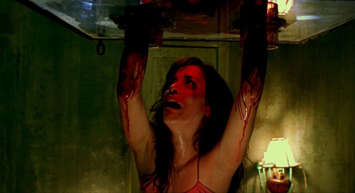 En kvinna har armarna i ett föremål fullt av rakhyvlar i Saw II, med blod som rinner nerför armarna.