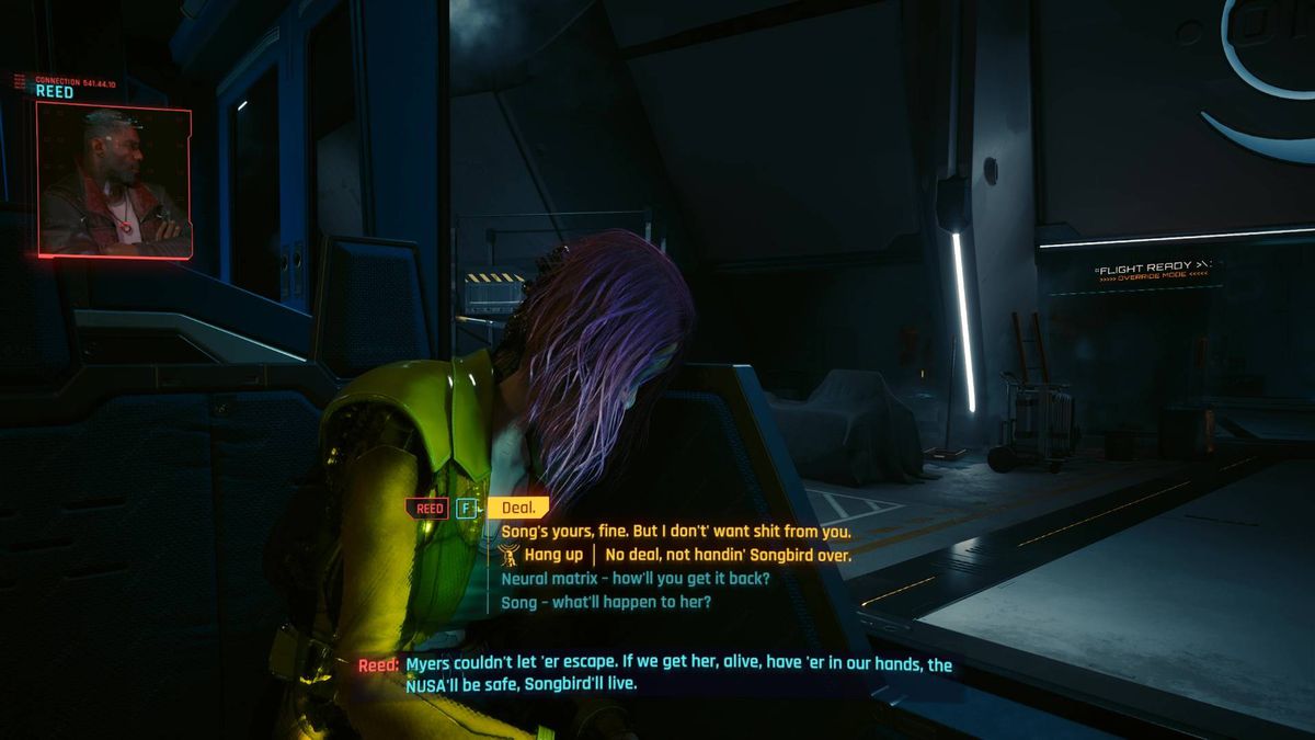 Songbird sitter vid ett skrivbord i ett mörkt rum under ett av Cyberpunk 2077 Phantom Liberty-sluten.