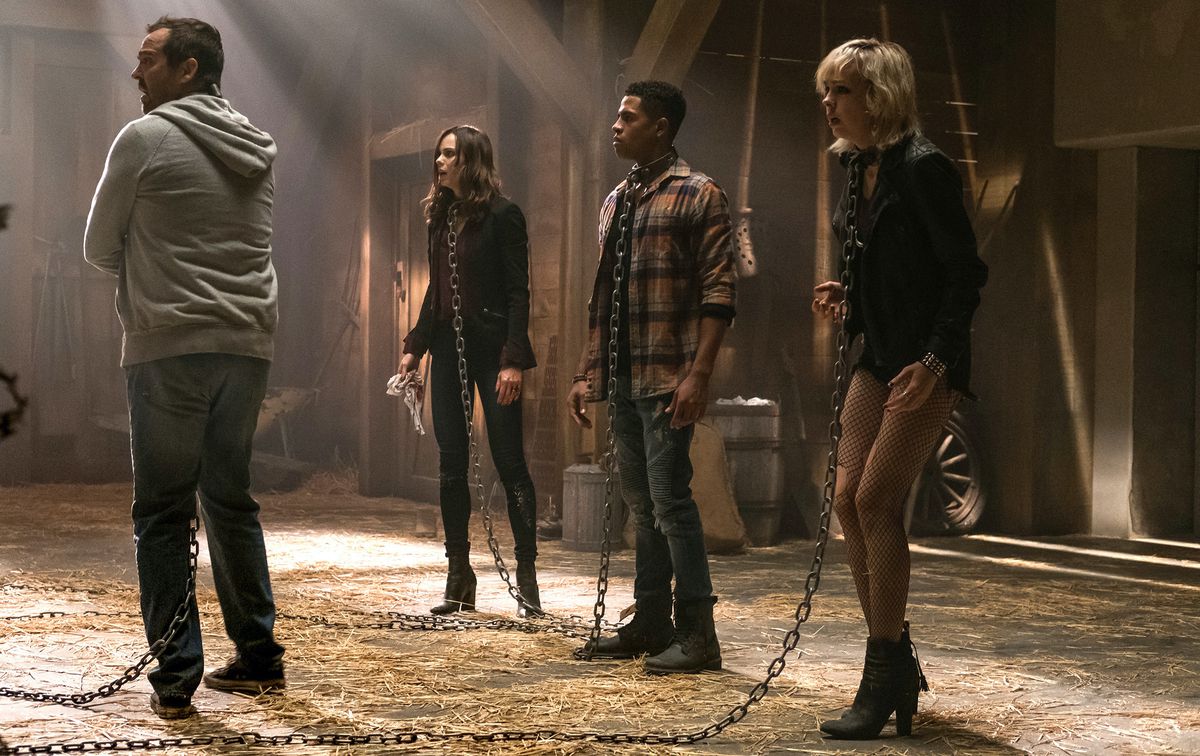 Four potential Jigsaw victims stand in a barn, wearing metal collars and long chains leading offscreen chains, in 2017’s Jigsaw