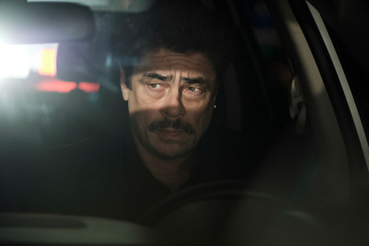 Benicio Del Toro som Tom Nichols sitter bakom ratten i ett fordon på natten med strålkastare som lyser genom hans bakfönster i Reptile.