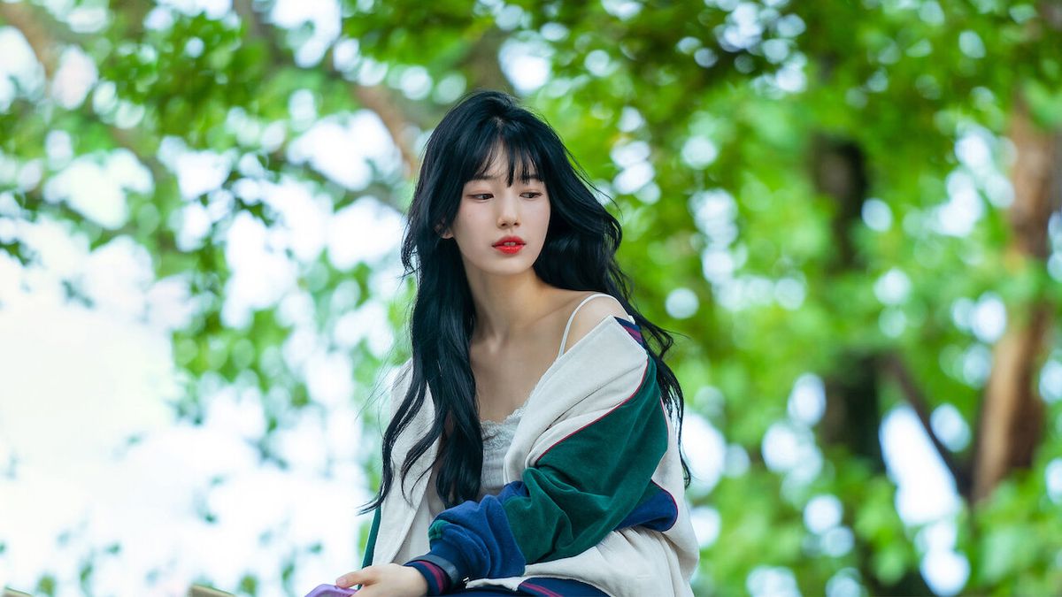 Bae Suzy ser kontemplativ ut i Doona!, klädd i en tröja som faller av axlarna när hon sitter ute i ett grönt område med träd.